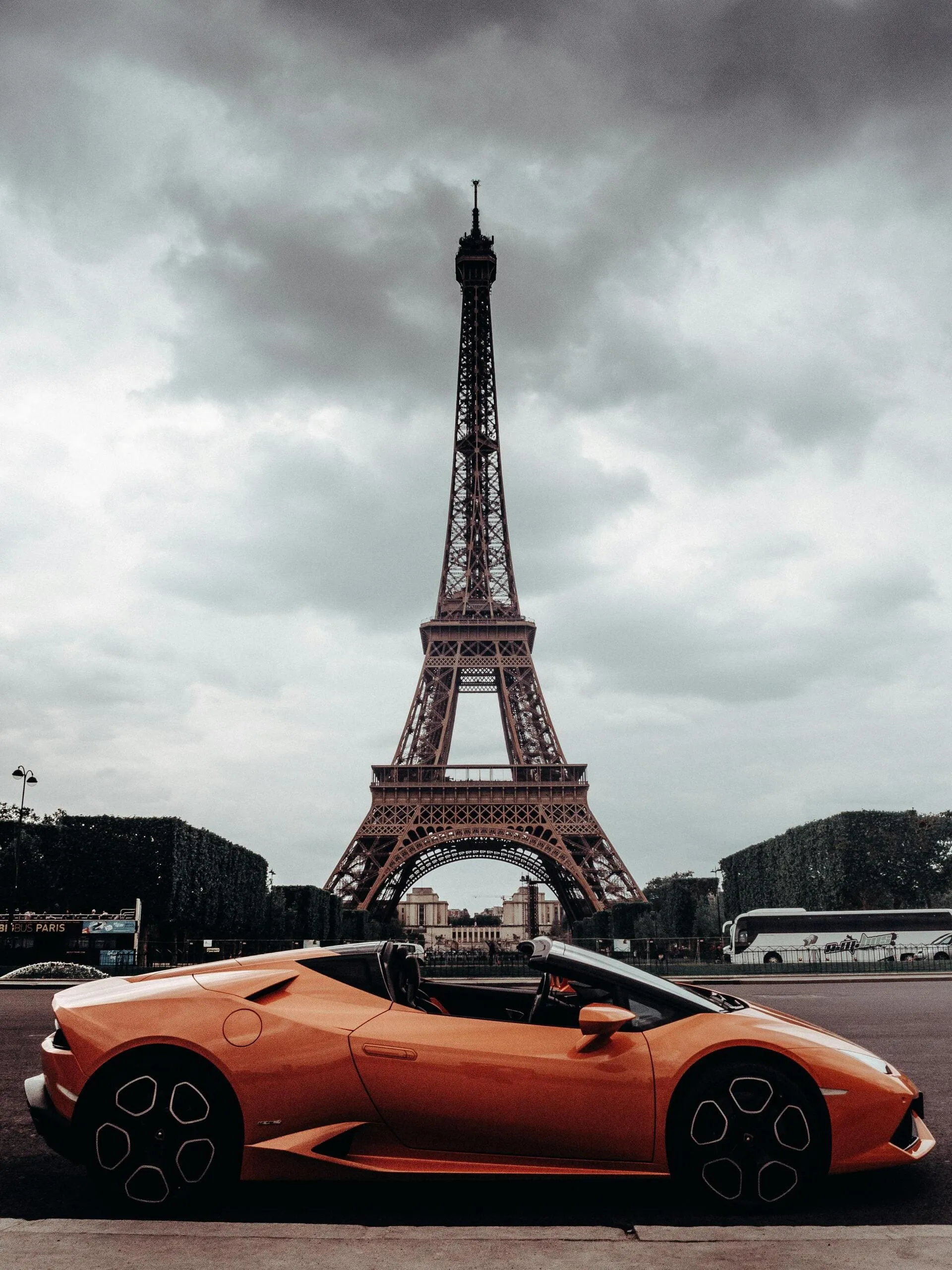 Voiture de sport orange devant la tour Eiffel.