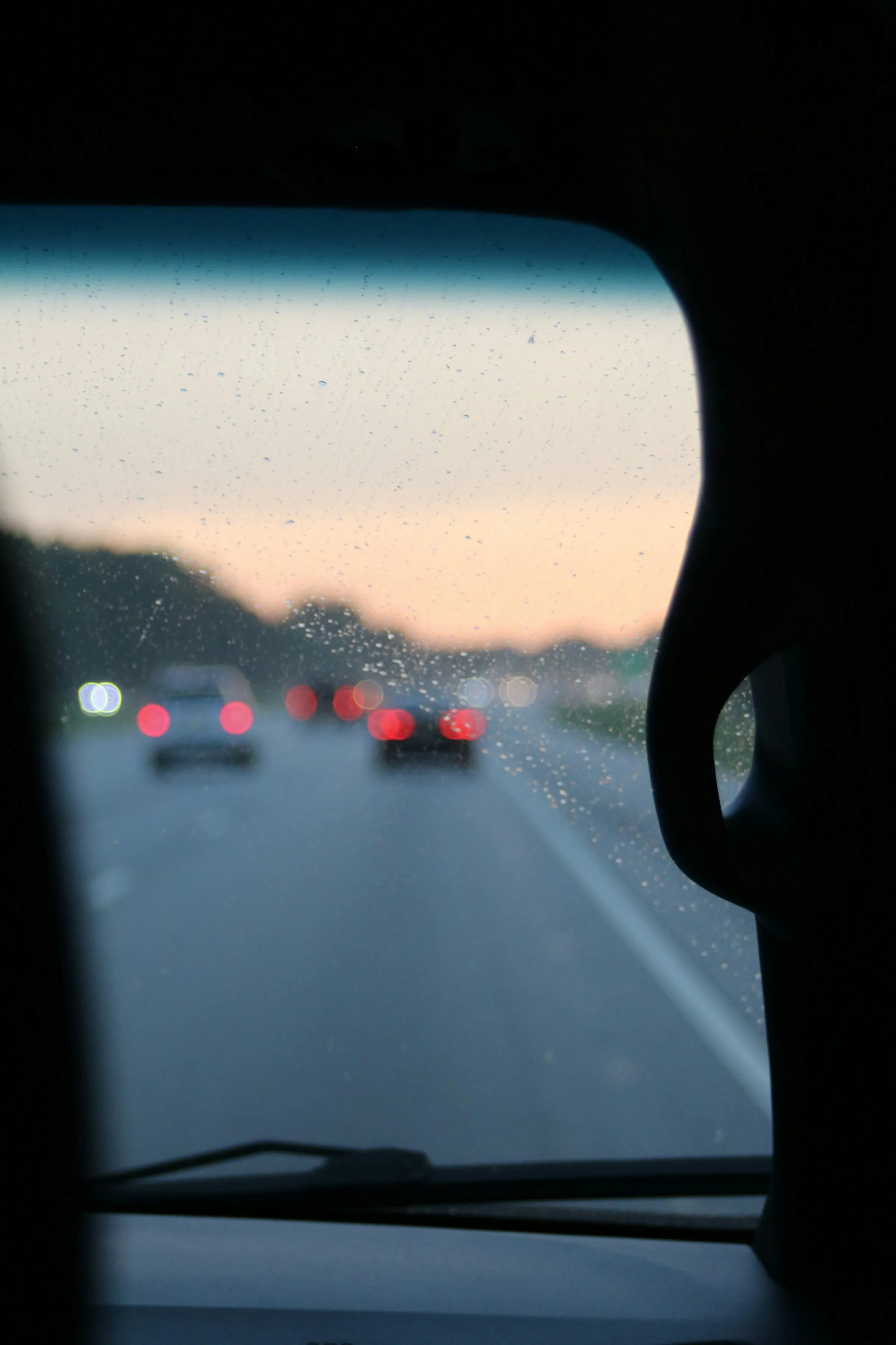 Gouttes sur une vitre de voiture, la route au crépuscule.